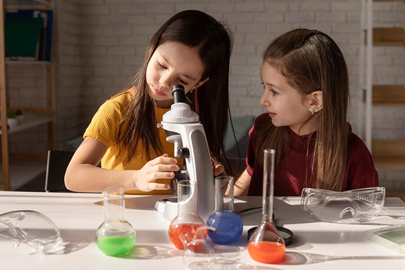 Two girls using a microscope and colorful lab equipment for science exploration.