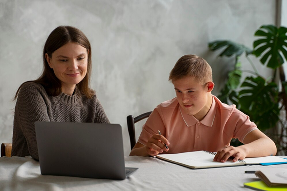 A woman helping a boy with homework using a laptop.