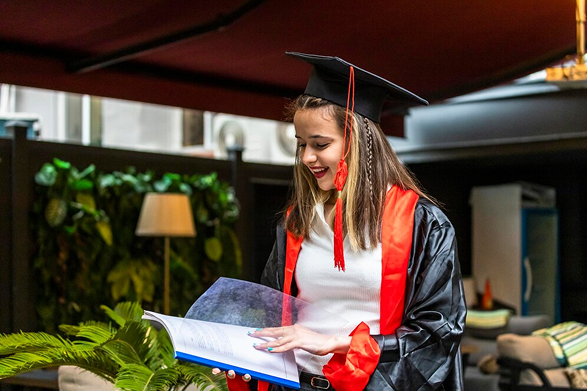 A happy graduate in cap and gown holding a diploma folder.