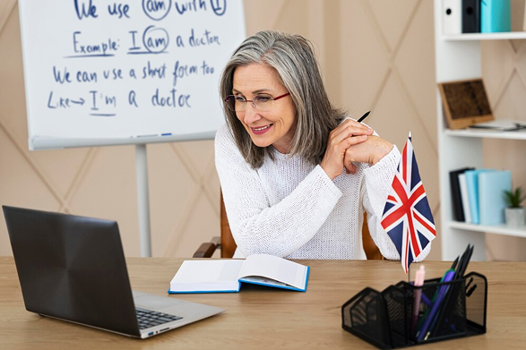 A woman teaching English online with a UK flag beside her laptop.