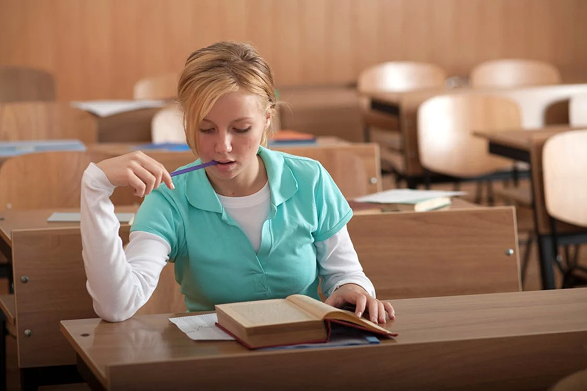 A student concentrating on writing in a classroom.