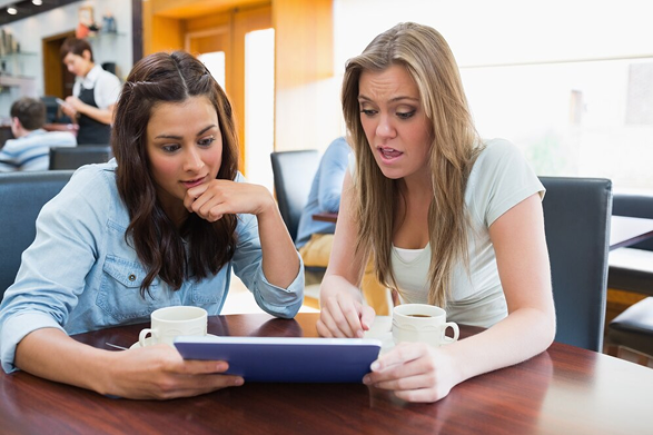 Two women intently looking at a tablet in a cozy cafe.