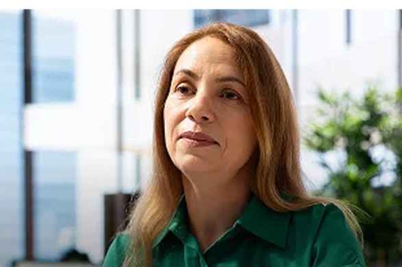 A confident woman with long hair wearing a green shirt indoors.