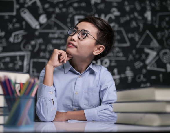 Student in glasses pondering in front of chalkboard with equations.
