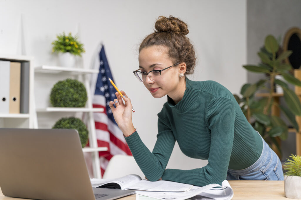 Young woman focused on a laptop, taking notes in a bright office space.